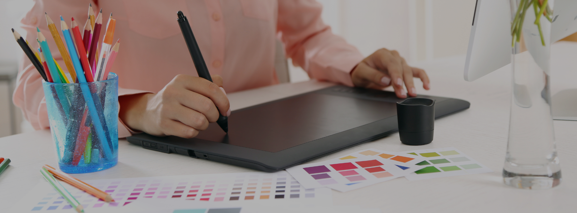 Designer desenhando em mesa digitalizadora com paletas de cores.